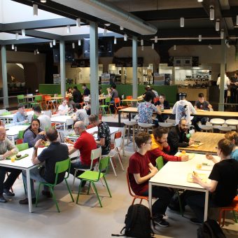 Groep studenten aan het werk achter de laptop in een grote zaal gelijk een hackathon.